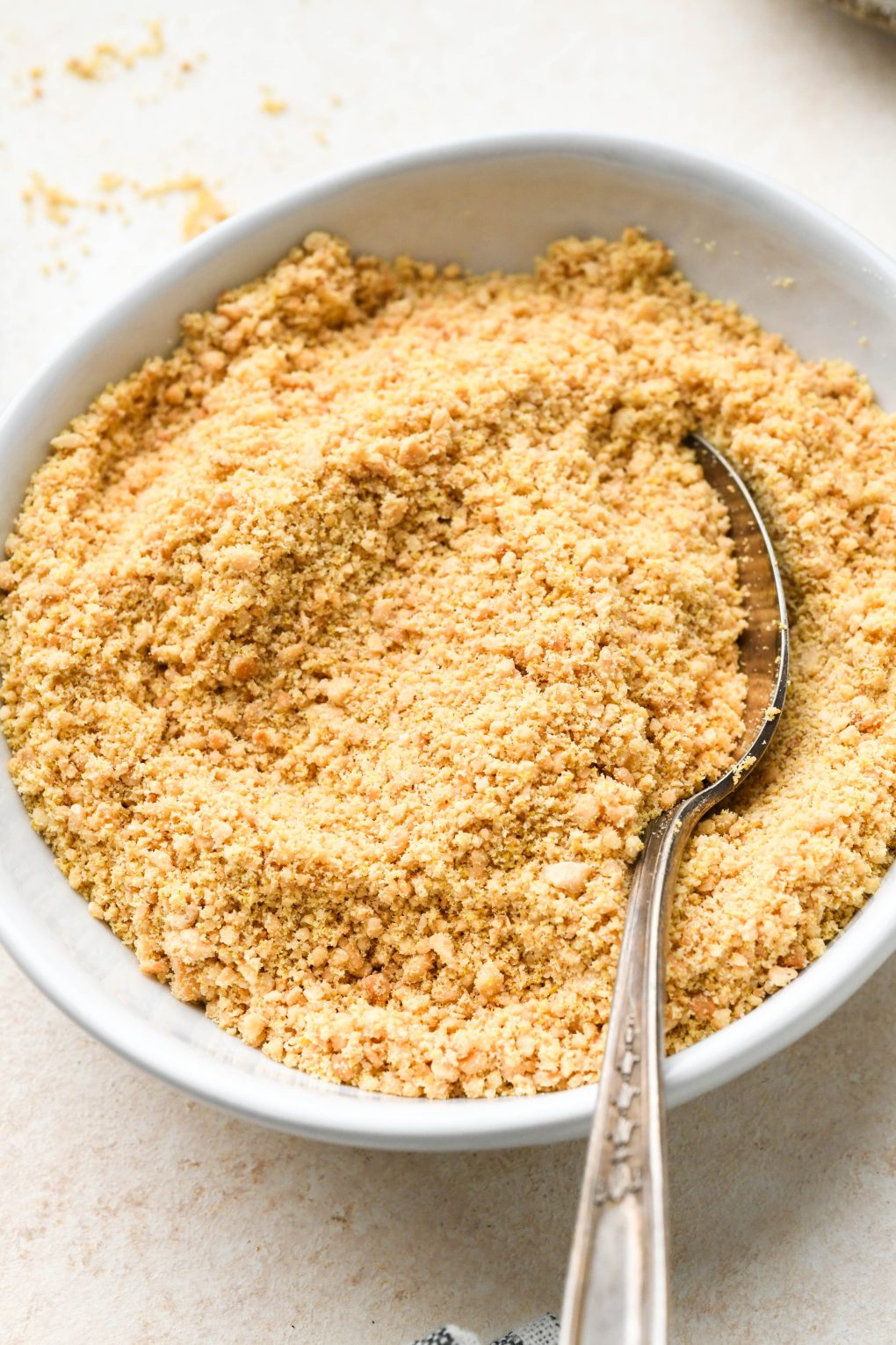 Vegan parmesan cheese in a small shallow white bowl, on a light cream colored background.