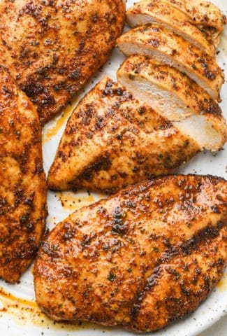 Four oven baked chicken breasts on a large speckled platter, one breast sliced into strips with the juicy interior showing.