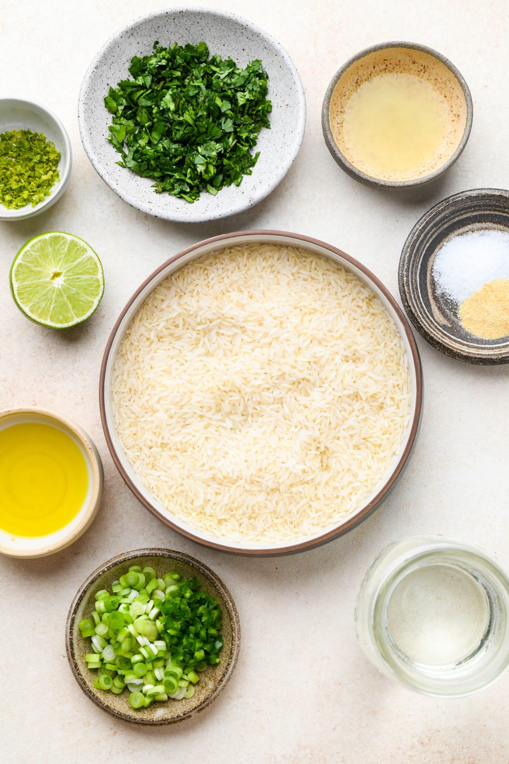 Cilantro lime rice ingredients in various sized ceramics on a light cream colored background.