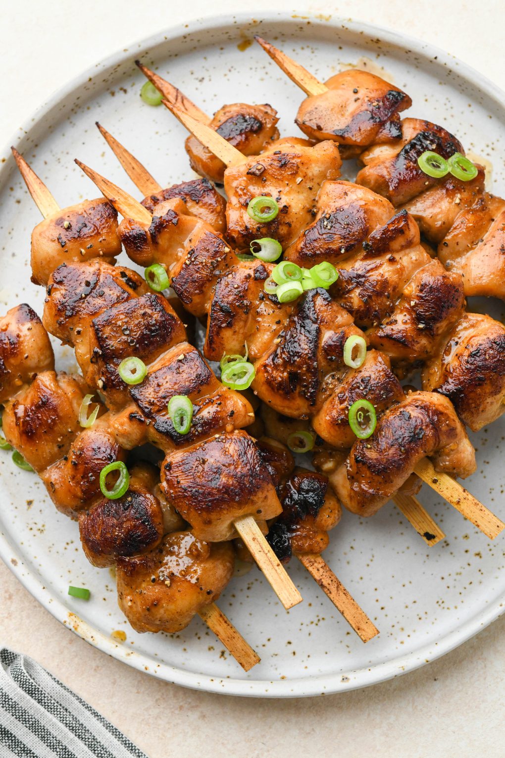 Cooked garlic ginger chicken skewers piled on a plate and topped with thinly sliced green onions.