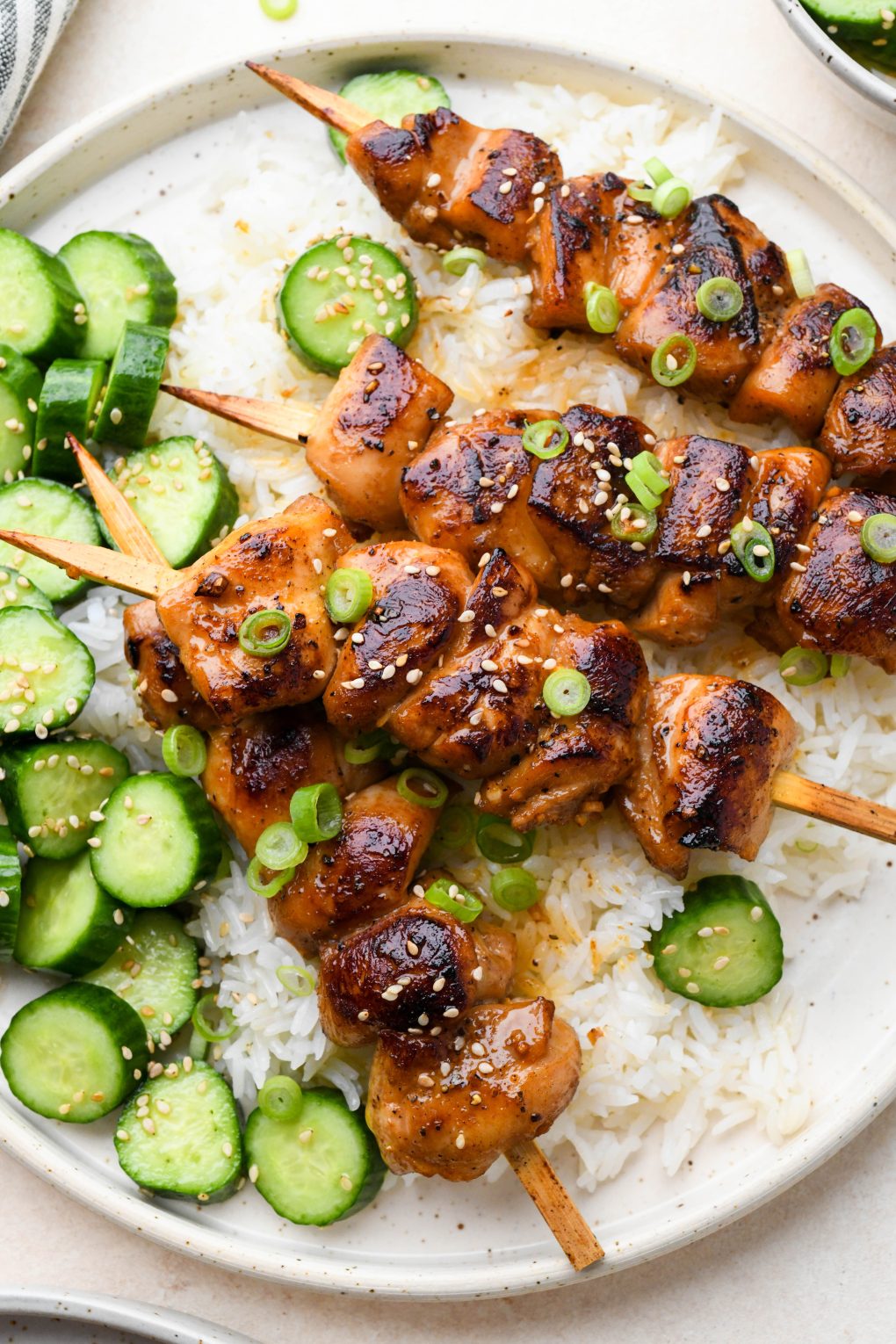 Grilled garlic ginger chicken skewers on top of white rice, next to an asian cucumber salad.