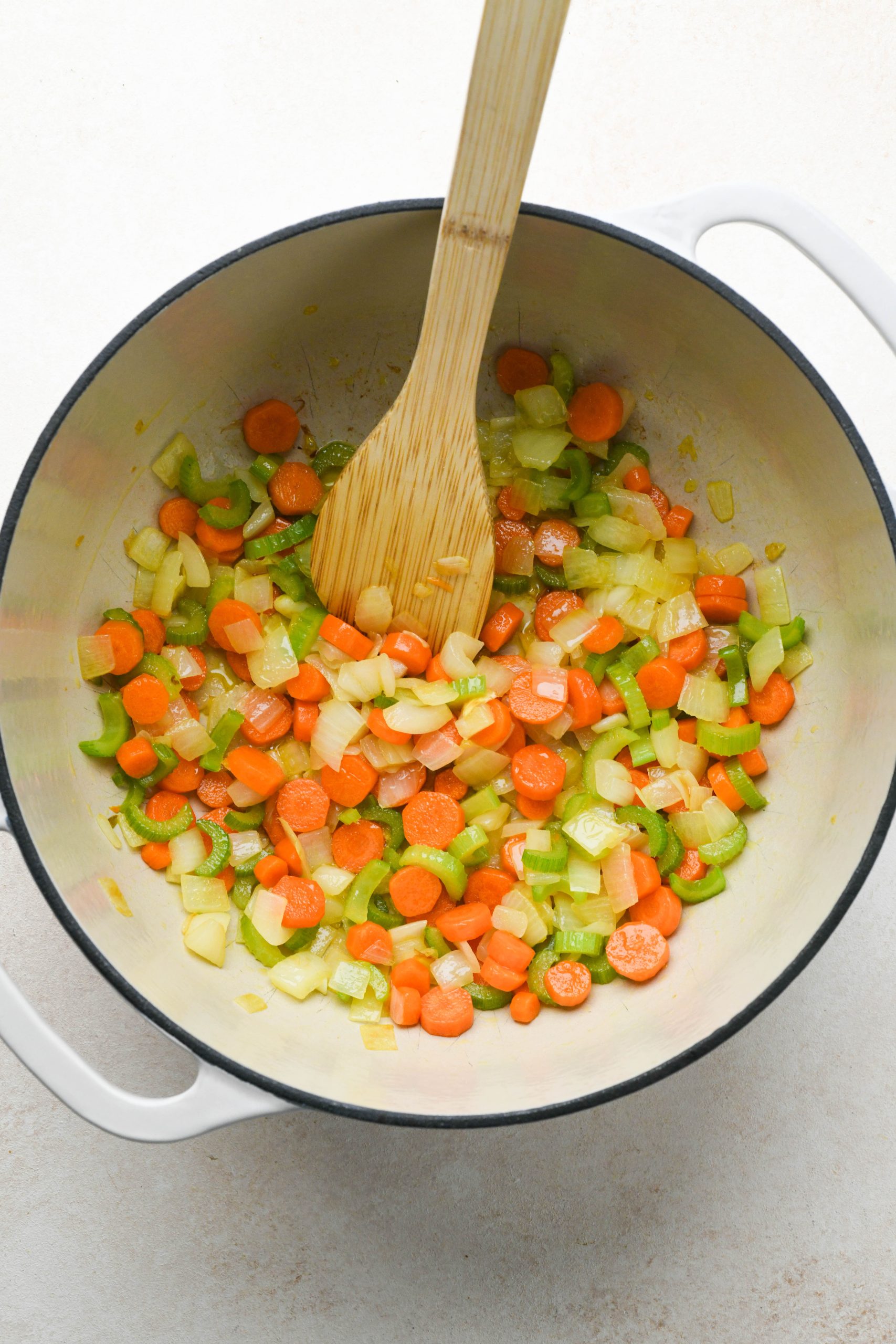 How to make chicken soup with spring vegetables: Carrots, onion, and celery sautéed in a large enameled soup pot.