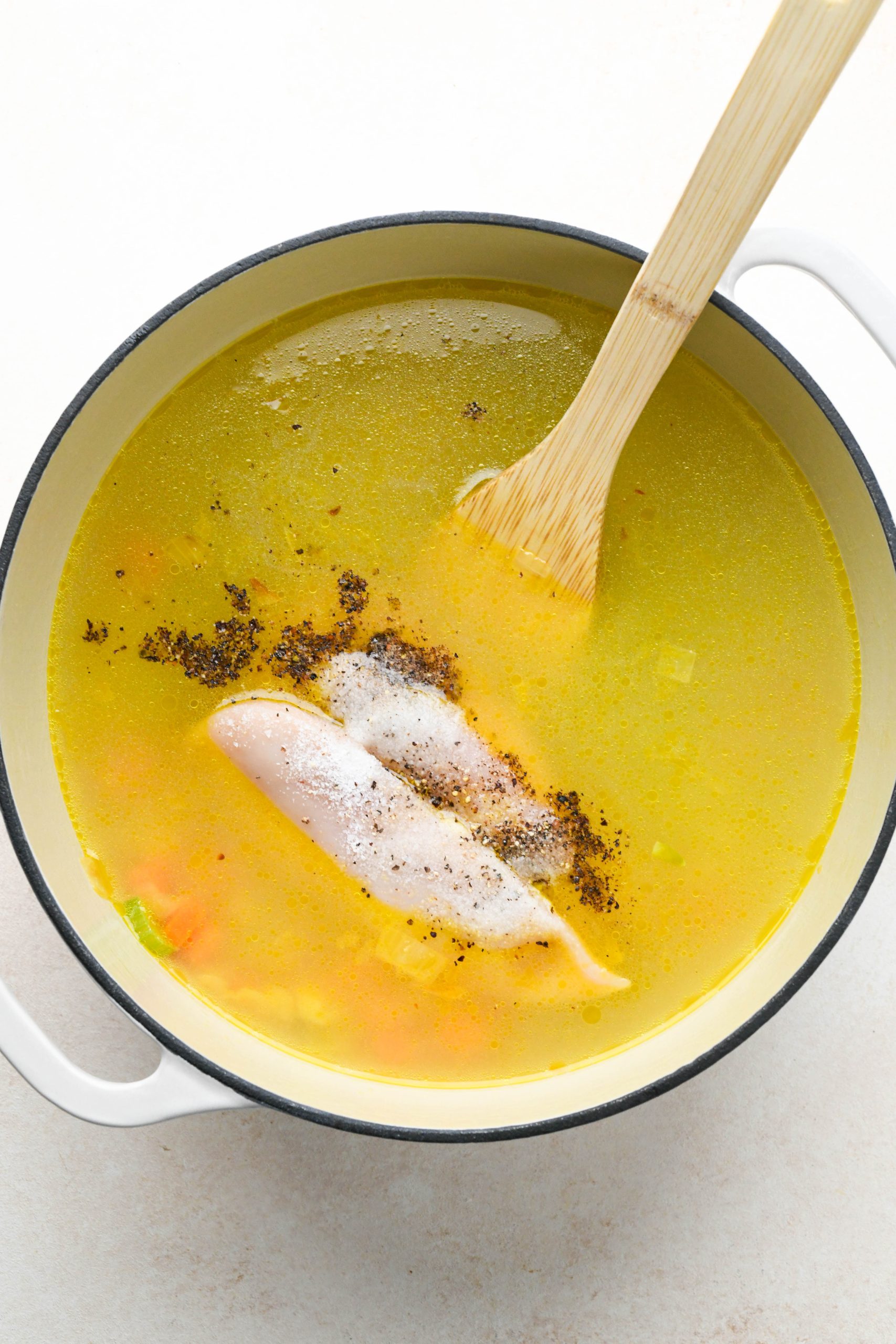 How to make chicken soup with spring vegetables: Broth, chicken, salt, and pepper added to the large enameled soup pot.