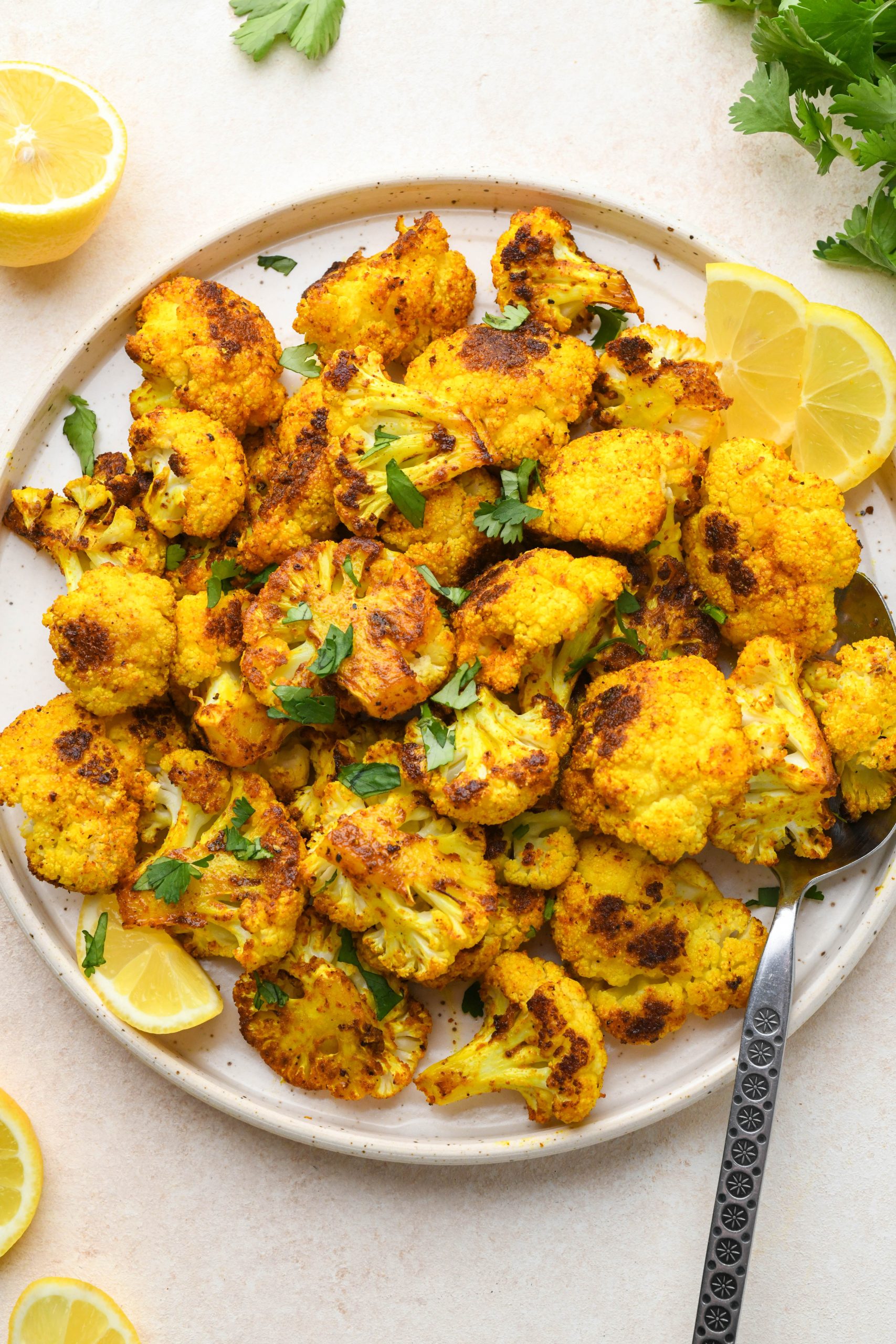 Turmeric roasted cauliflower on a speckled ceramic plate topped with fresh herbs.