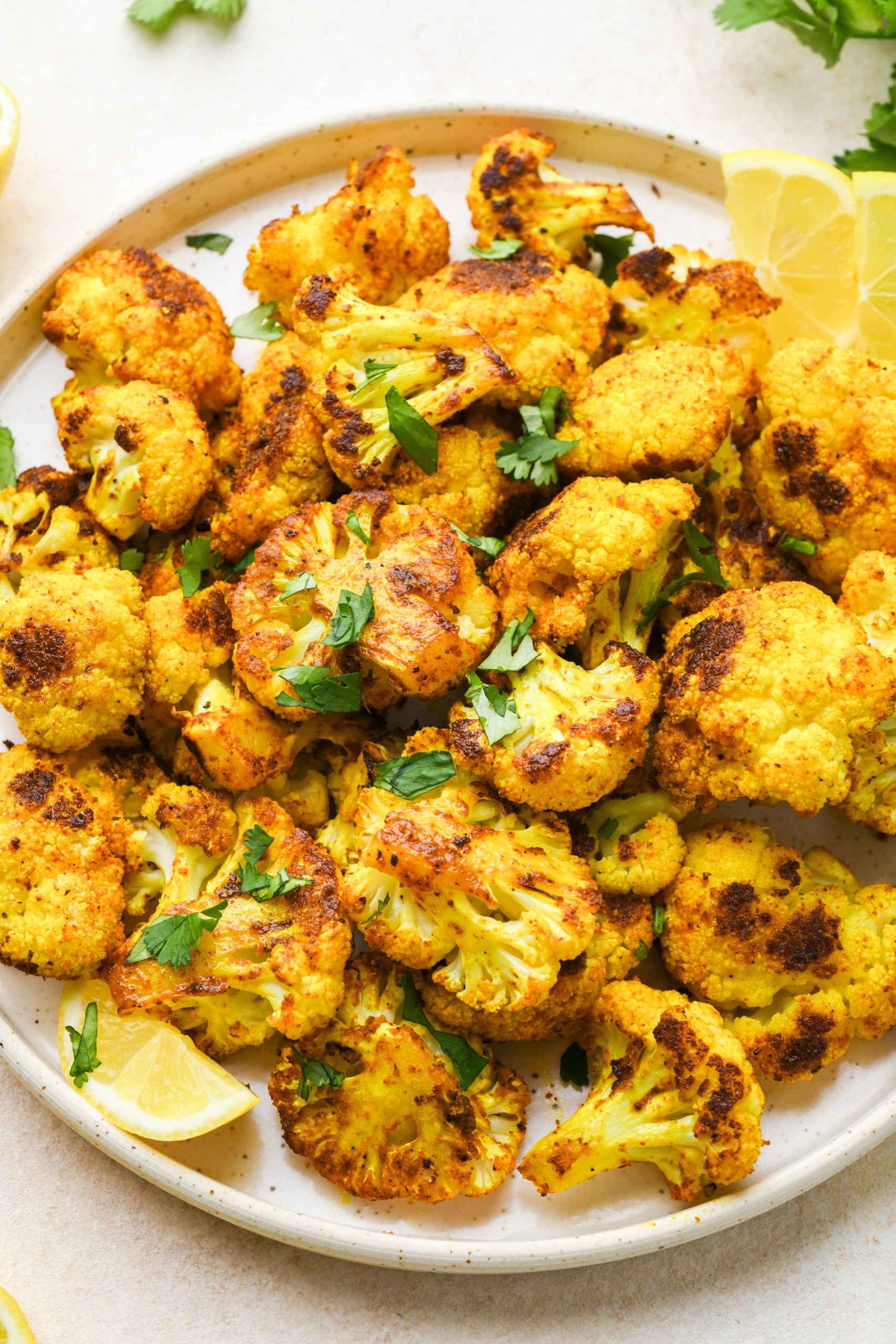 Turmeric roasted cauliflower on a speckled ceramic plate topped with fresh herbs.