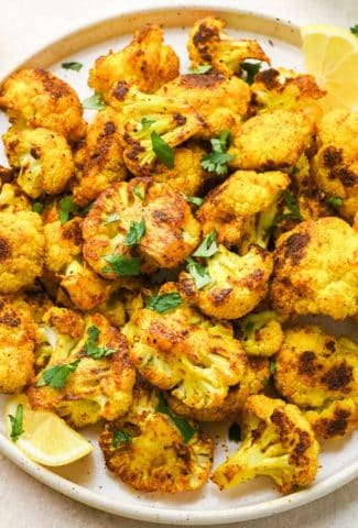 Turmeric roasted cauliflower on a speckled ceramic plate topped with fresh herbs.