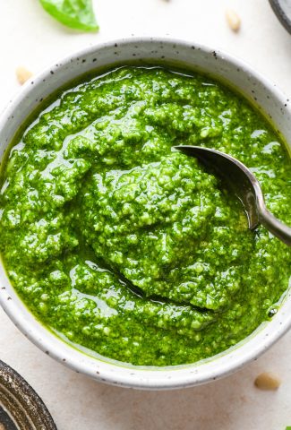 Homemade basil pesto in a small speckled bowl with a spoon dipping in.