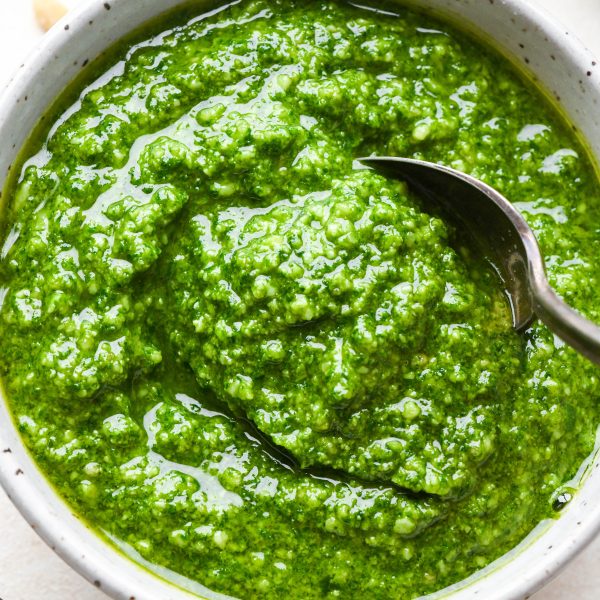 Homemade basil pesto in a small speckled bowl with a spoon dipping in.