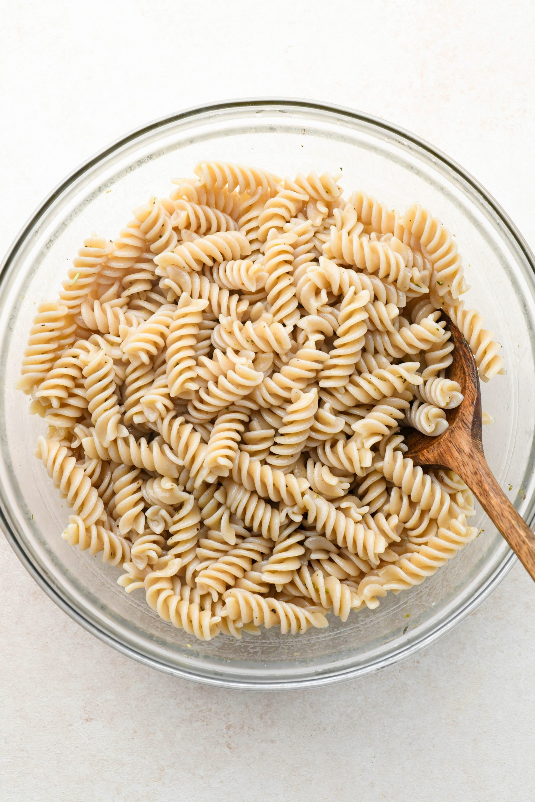 How to make Easy Gluten Free Italian Pasta Salad: Cooked fusilli pasta in a large glass bowl, tossed with some of the dressing.