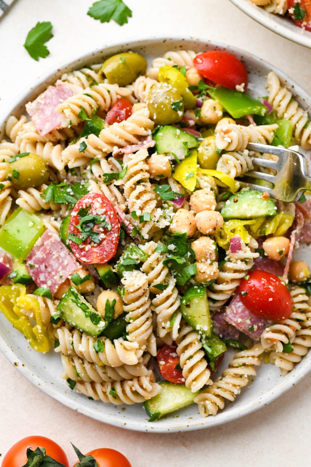 A small plate of Italian pasta salad with a fork digging into take a bite.