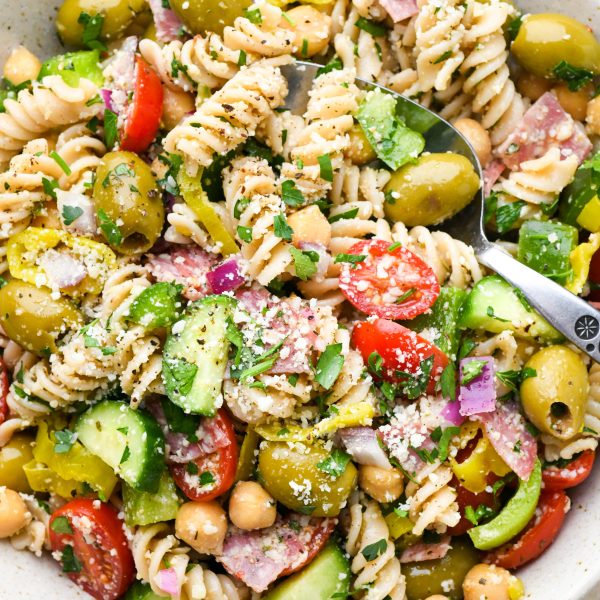 Close up image of easy gluten free Italian pasta salad with fresh ingredients like tomatoes, cucumbers, red onion, olives, herbs, and parmesan cheese.