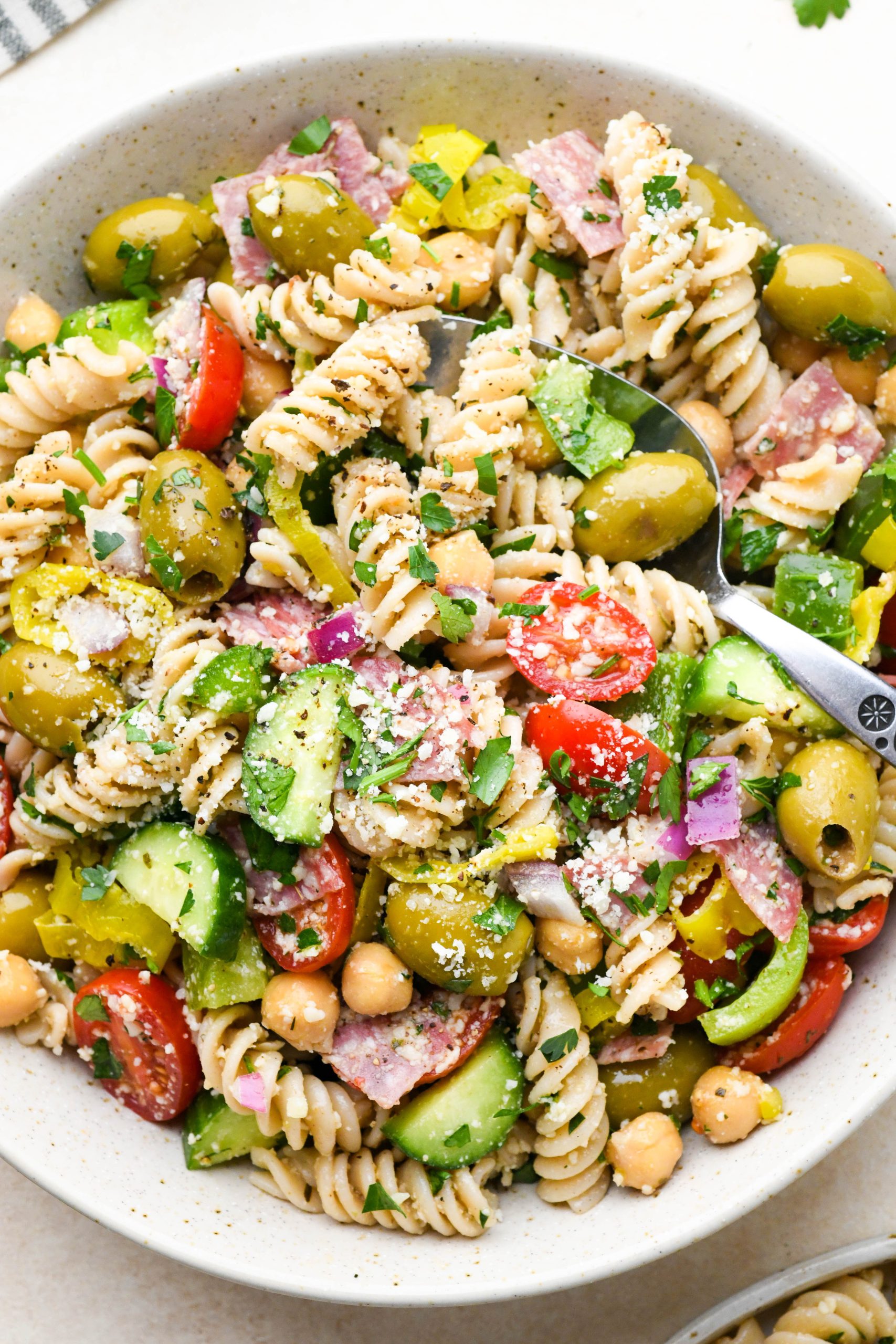 Close up image of easy gluten free Italian pasta salad with fresh ingredients like tomatoes, cucumbers, red onion, olives, herbs, and parmesan cheese.