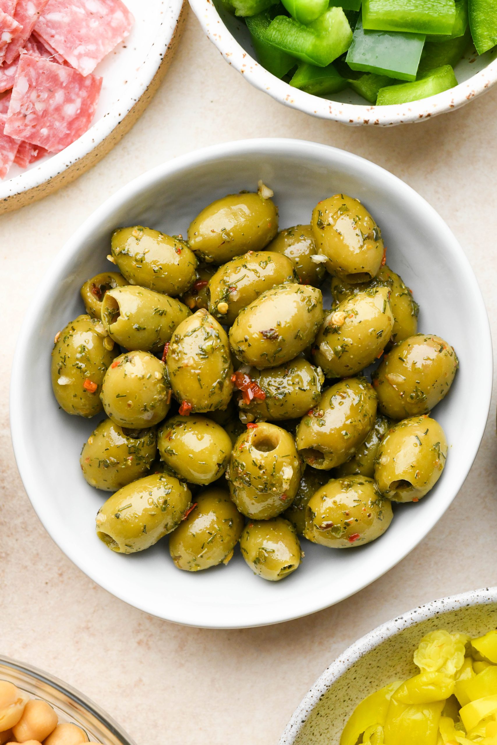 Herby olives in a small white ceramic bowl on a cream colored background.