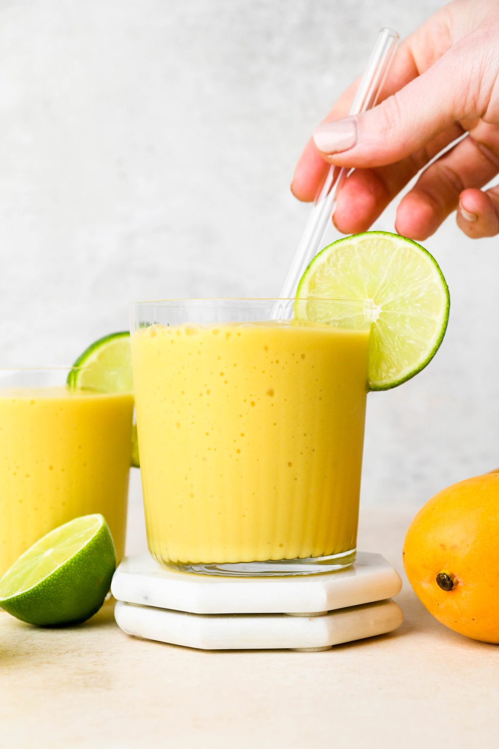 A hand placing a glass straw in a glass of mango smoothie.