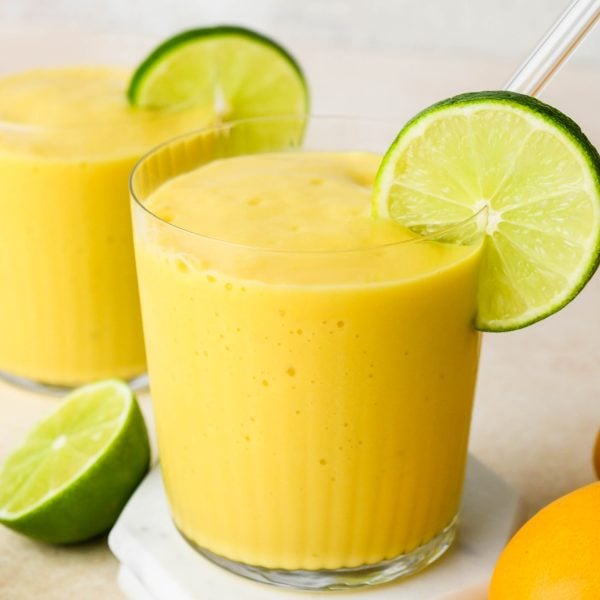 Mango smoothie in a glass with a glass straw, garnished with a lime wheel.