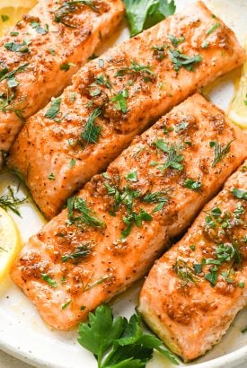 Perfectly cooked baked salmon filets on a cream colored plate, topped with fresh herbs.