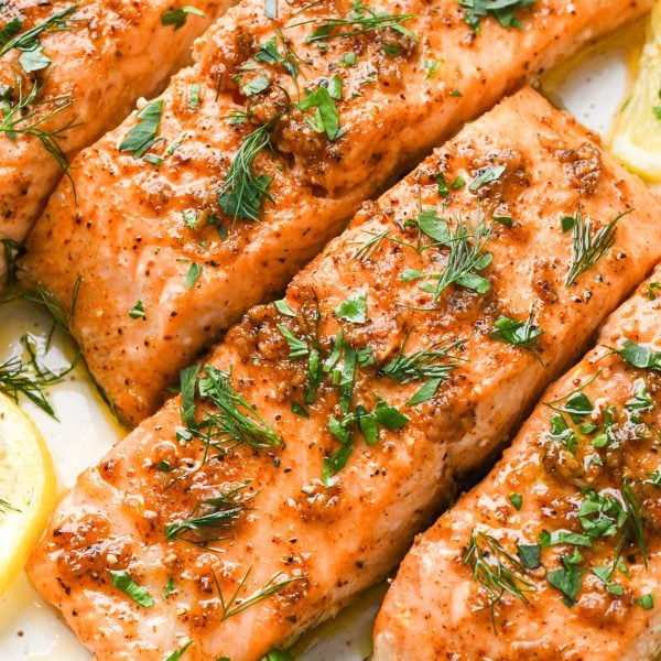 Perfectly cooked baked salmon filets on a cream colored plate, topped with fresh herbs.