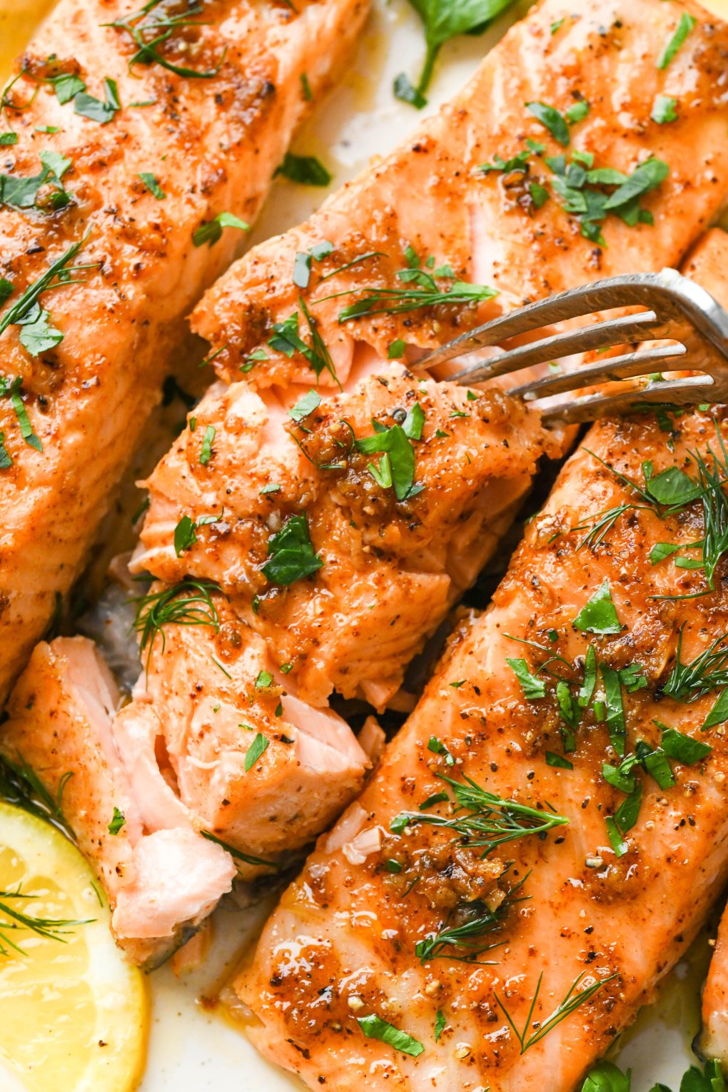 Close up of a plate of perfectly cooked salmon filets, a bite flaked out with a fork.