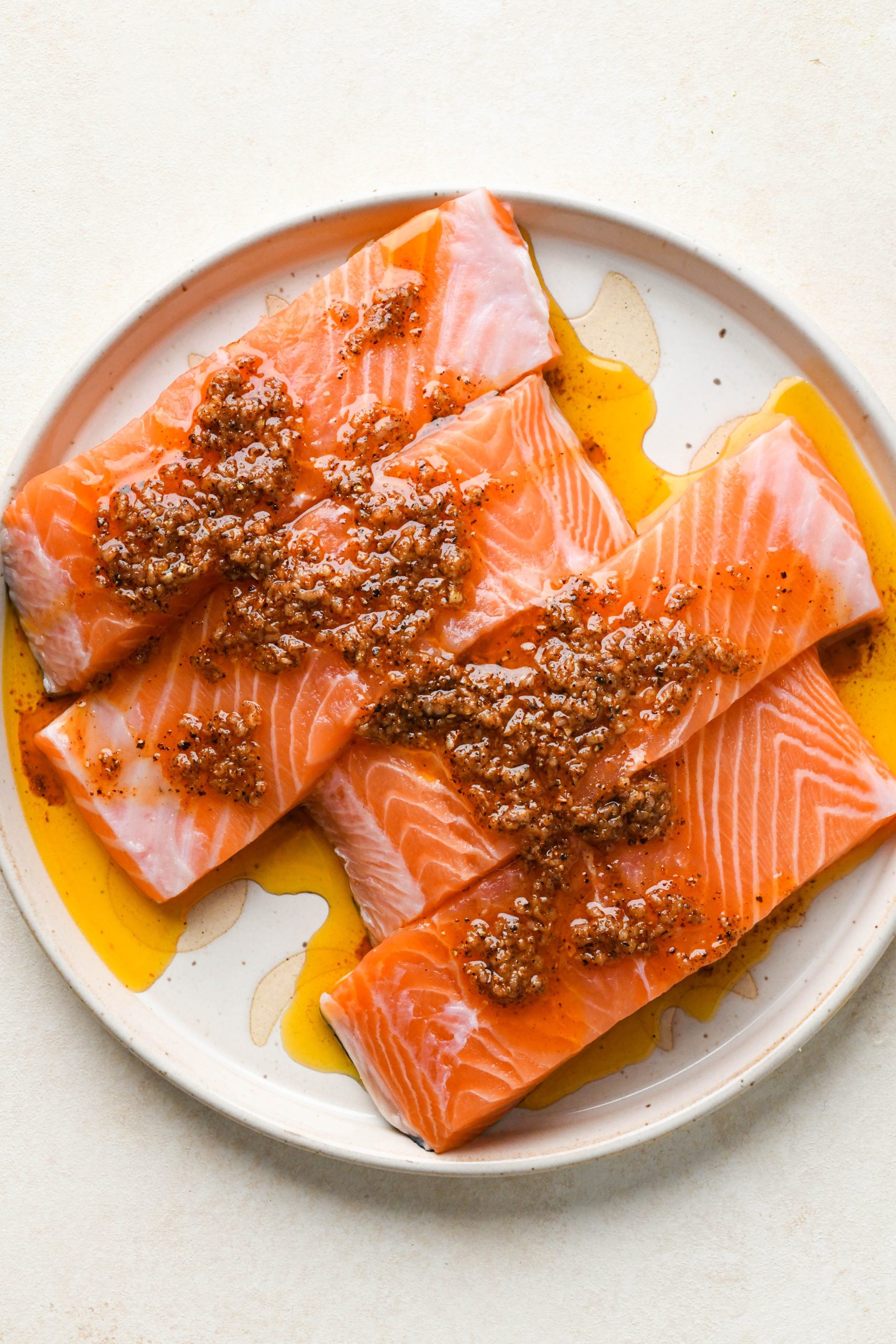 How to make baked salmon: Salmon fillets on a ceramic plate drizzled with avocado oil and spice mixture.