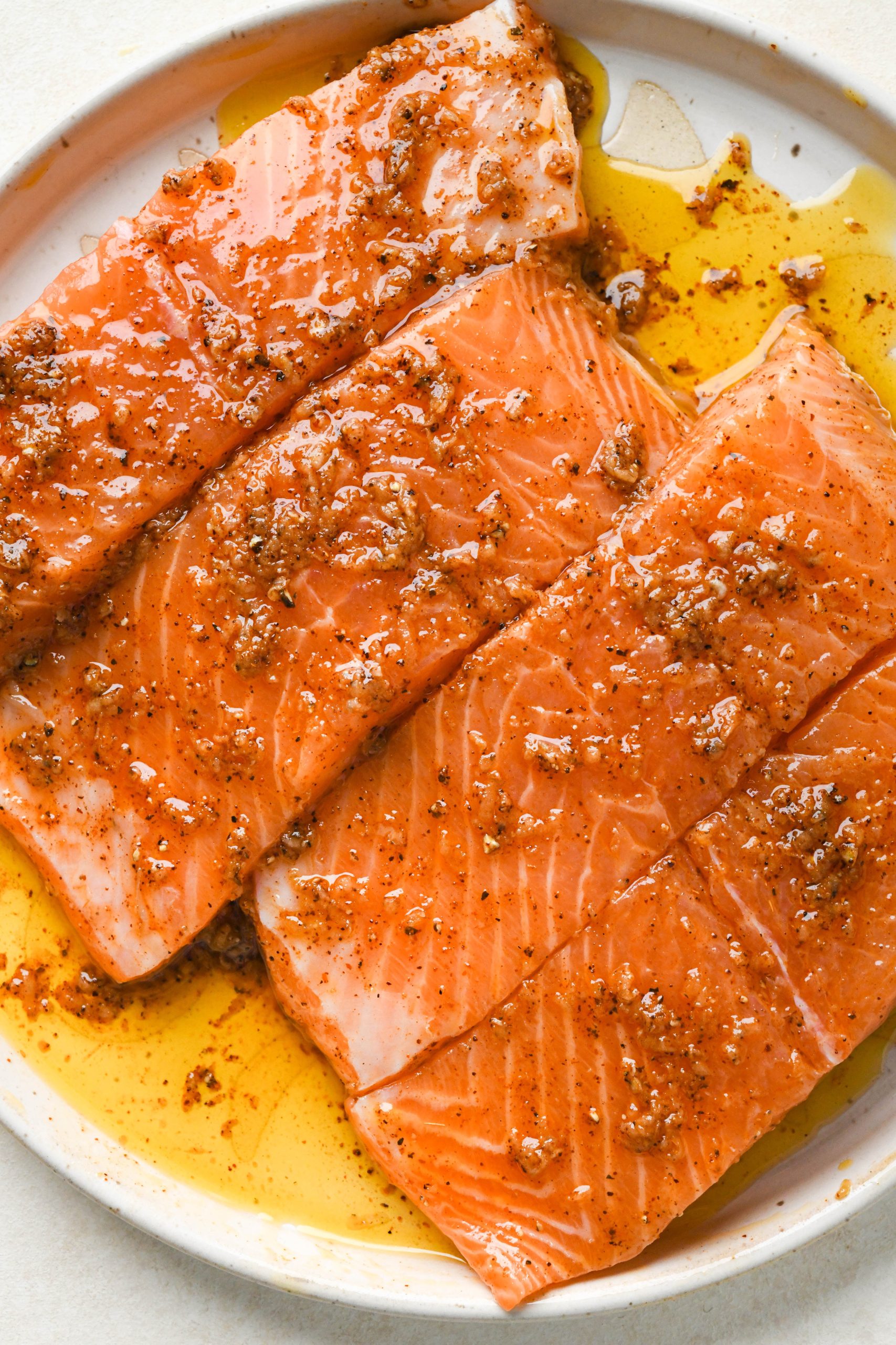 How to make baked salmon: Salmon fillets on a ceramic plate coated with avocado oil and spice mixture.