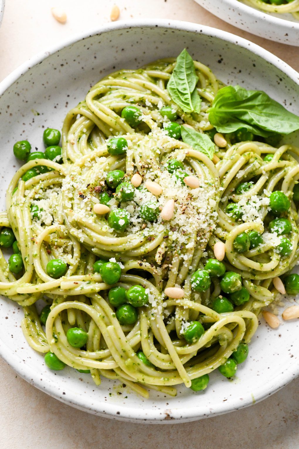 Pesto pasta made with spaghetti twirled in a speckled ceramic bowl and topped with pine nuts and grated parmesan.