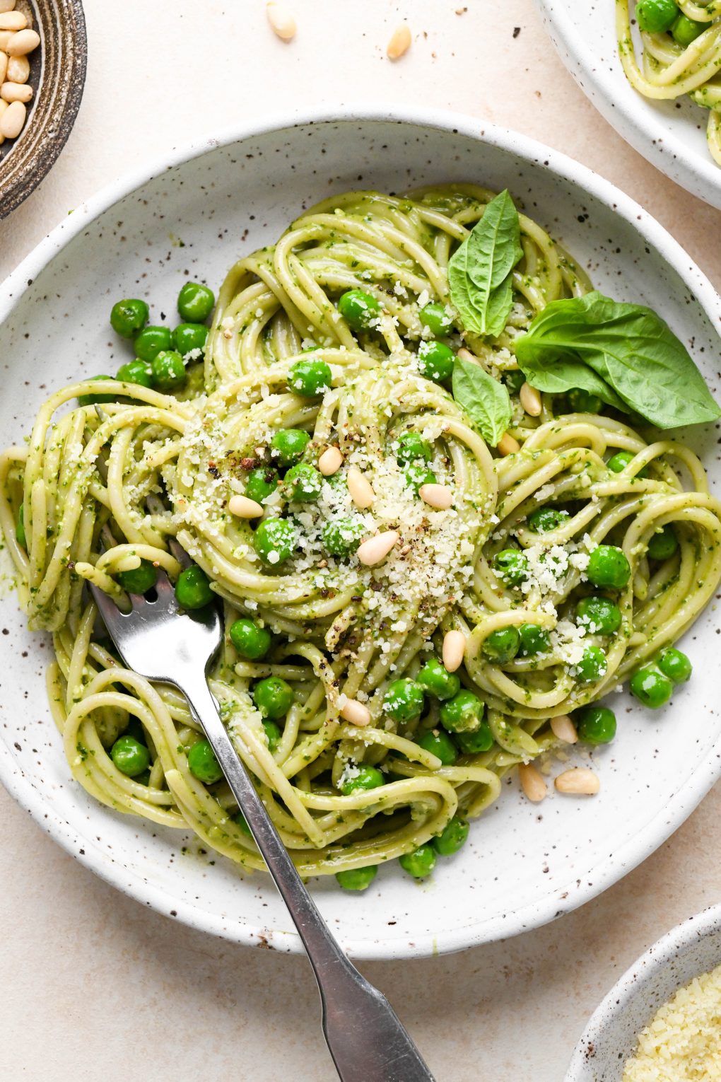 Pesto pasta made with spaghetti twirled in a speckled ceramic bowl and topped with pine nuts and grated parmesan.