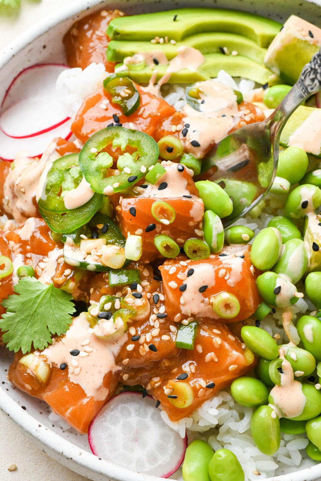Close up image of a fork picking up a bite of homemade poke bowl topped with spicy mayo and sesame seeds.