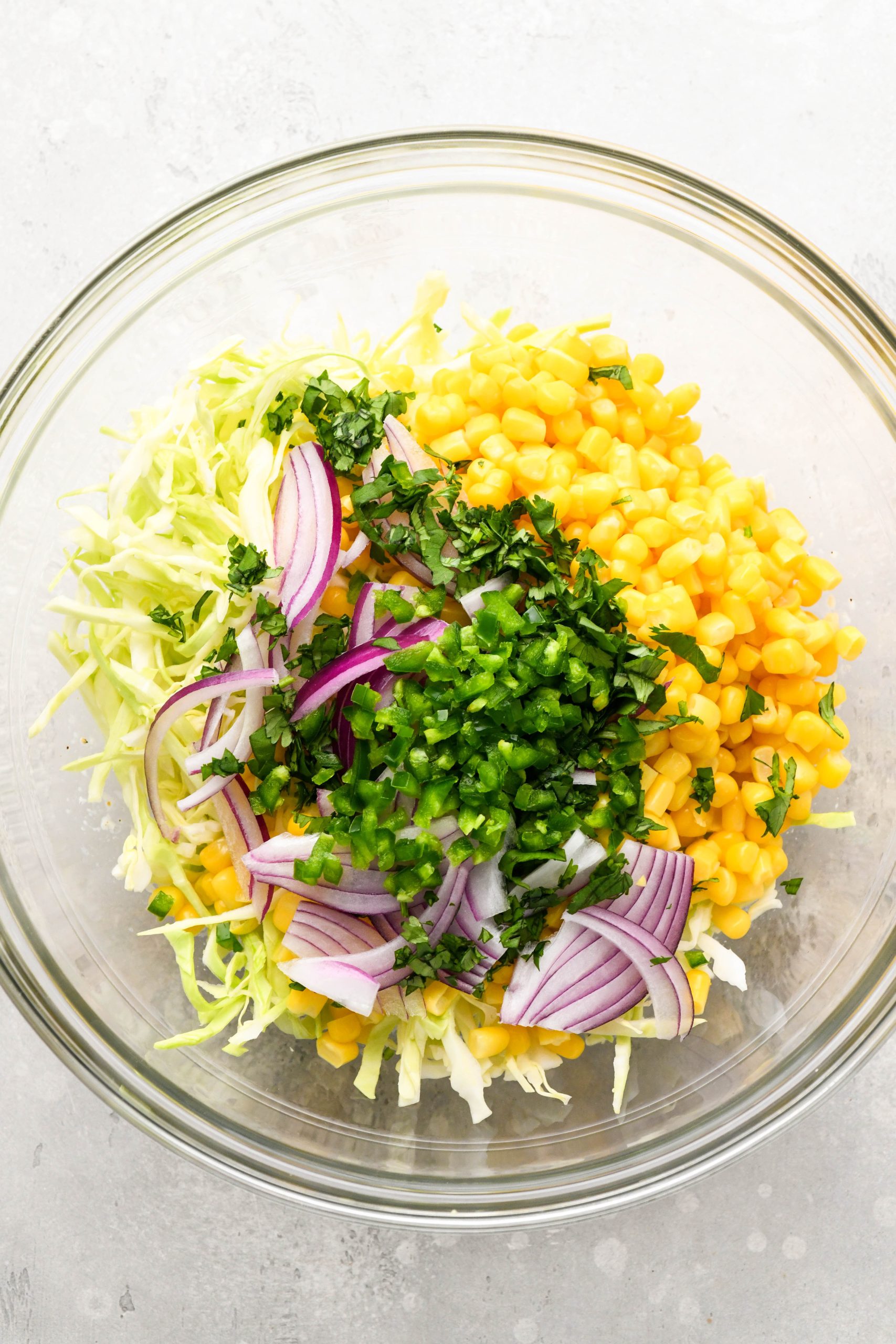 How to make ground pork tacos with creamy slaw: Fresh ingredients added to the large glass bowl with the creamy dressing before mixing.