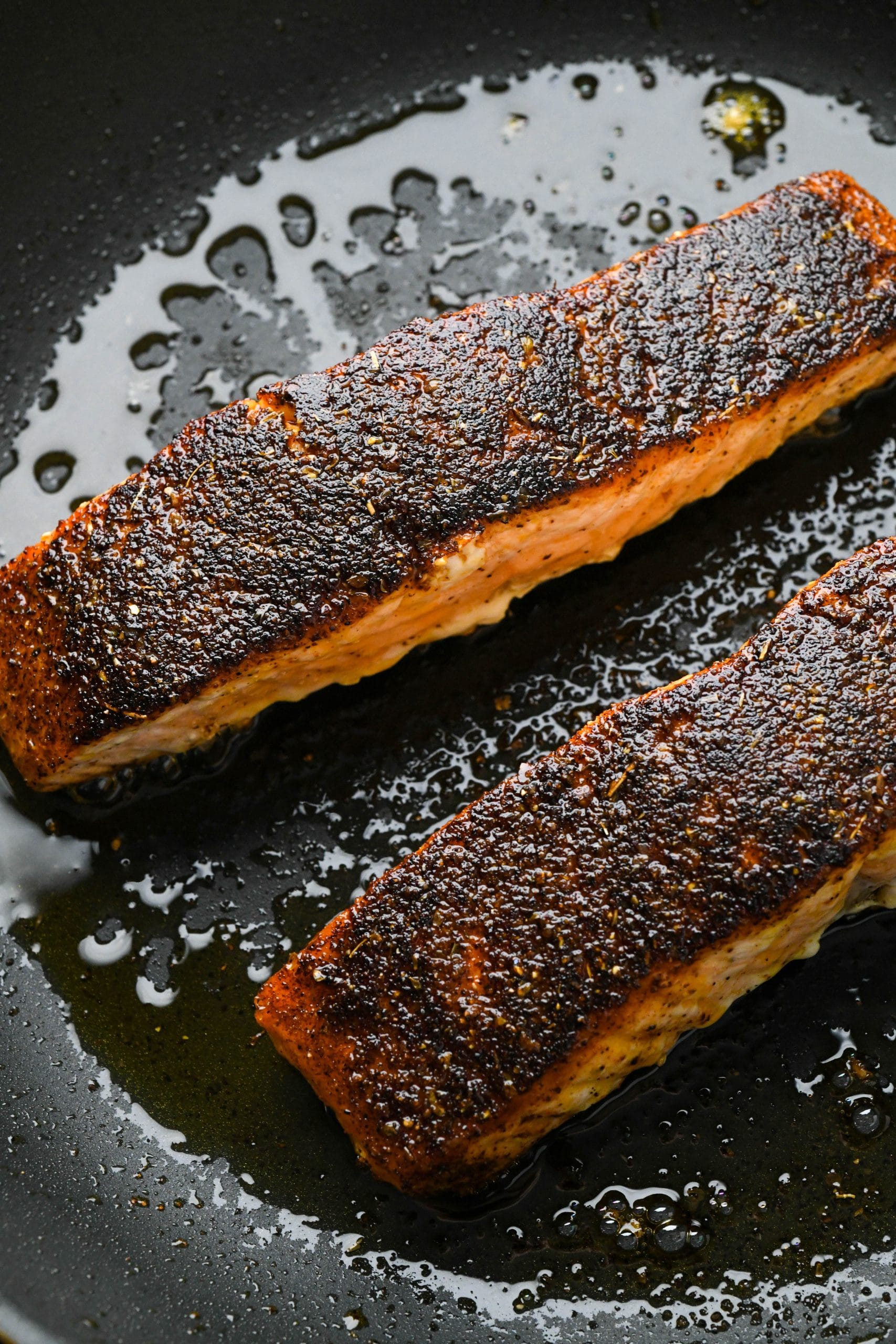 Cooked blackened salmon filets in a small skillet.
