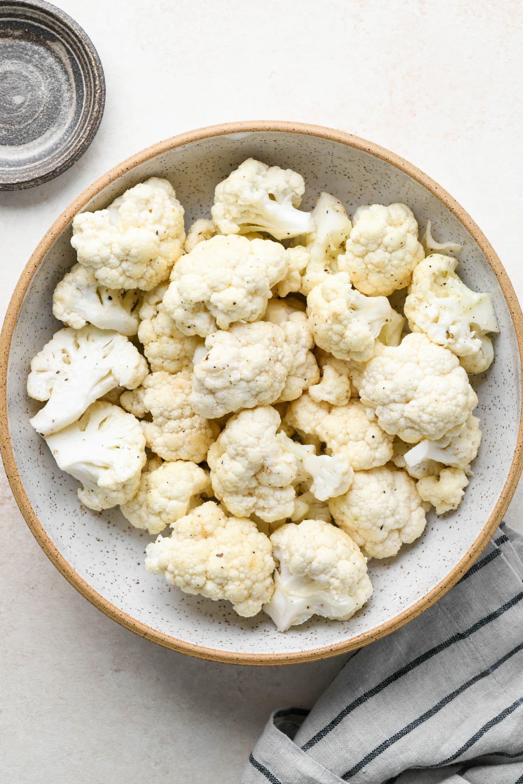 How to make buffalo cauliflower: Raw cauliflower florets in a bowl tossed with oil and spices.