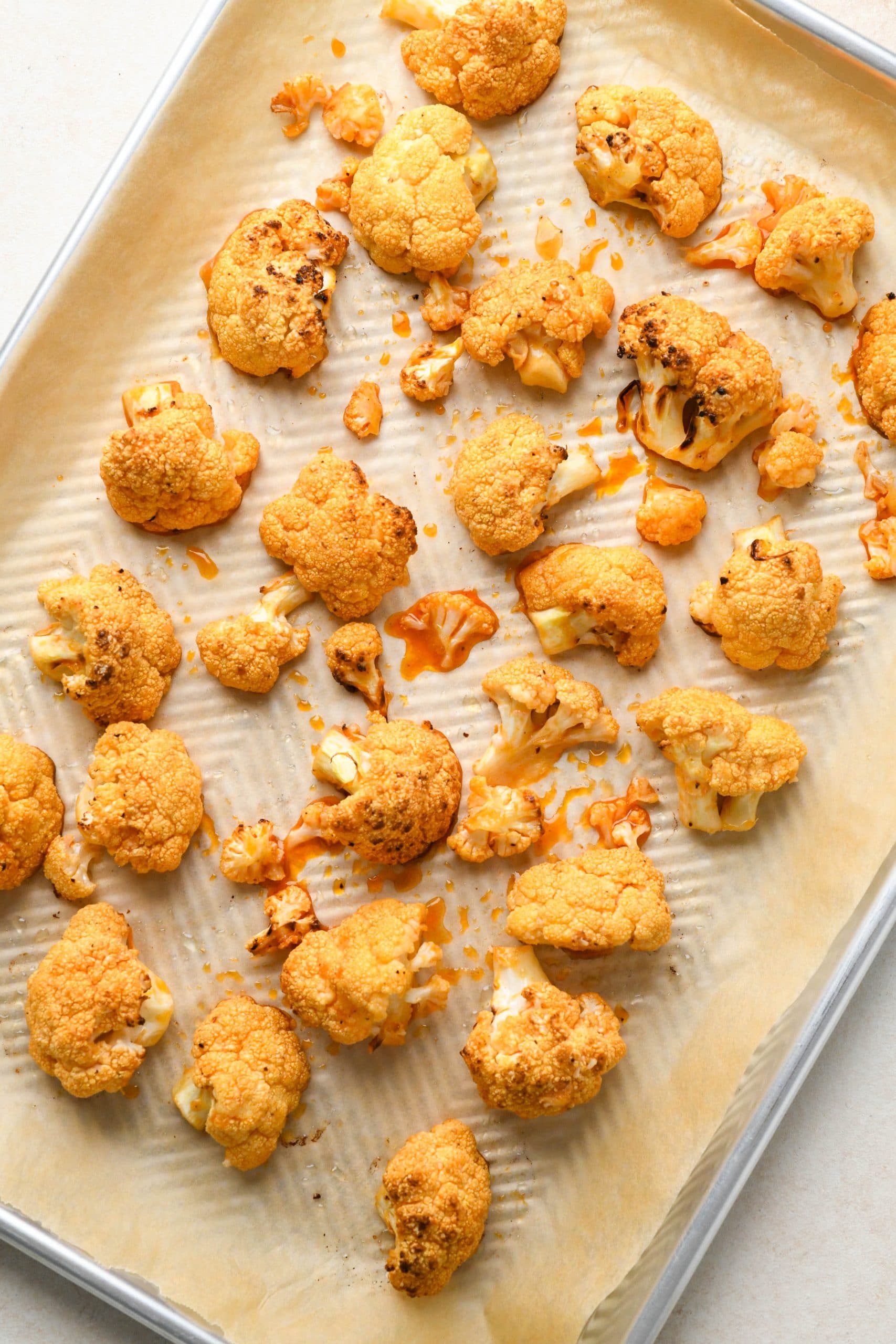 How to make buffalo cauliflower: Roasted cauliflower florets tossed with buffalo sauce and spread out on sheet pan.