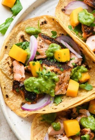 A trio of blackened salmon tacos on a large white speckled plate.