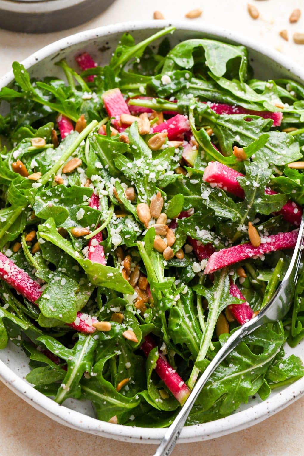 Simple arugula salad with thinly sliced watermelon radish on a small white speckled plate.