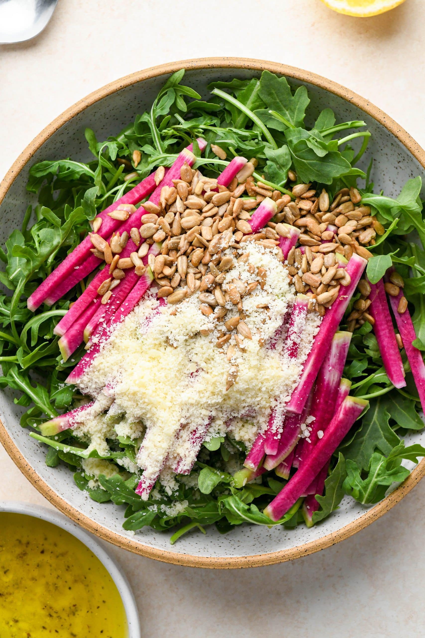 How to make Simple Arugula Salad: Arugula in a large bowl topped with julienned watermelon radish, sunflower seeds, and grated parmesan.