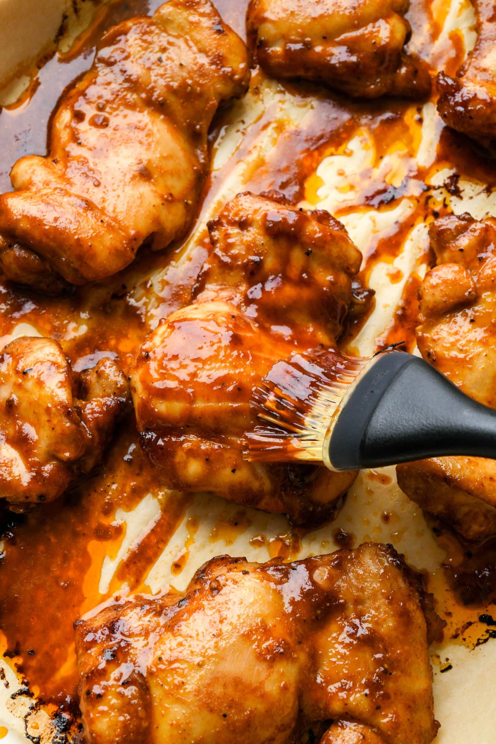 How to make BBQ Chicken Thighs in the Oven: Brushing a partially baked chicken thigh with extra bbq sauce.