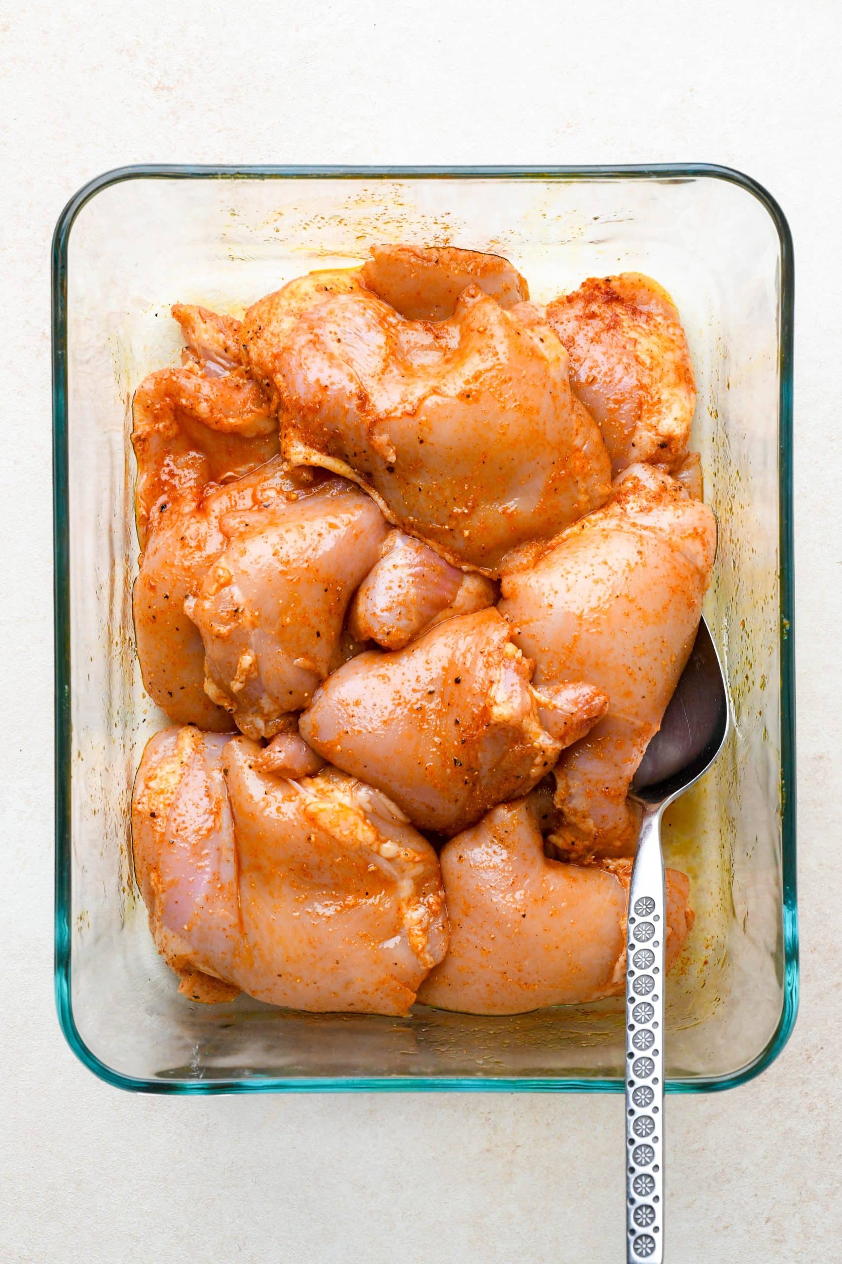 How to make BBQ Chicken Thighs in the Oven: Chicken thighs in a glass container mixed together with oil and spices.