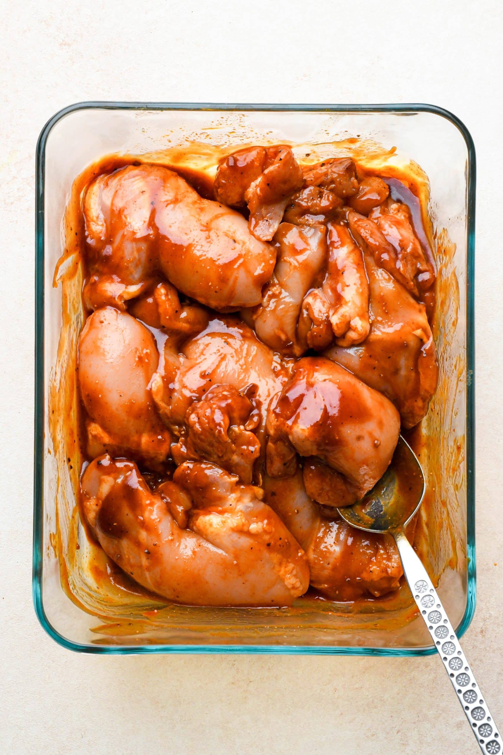 How to make BBQ Chicken Thighs in the Oven: Chicken thighs in a glass container mixed together with bbq sauce.