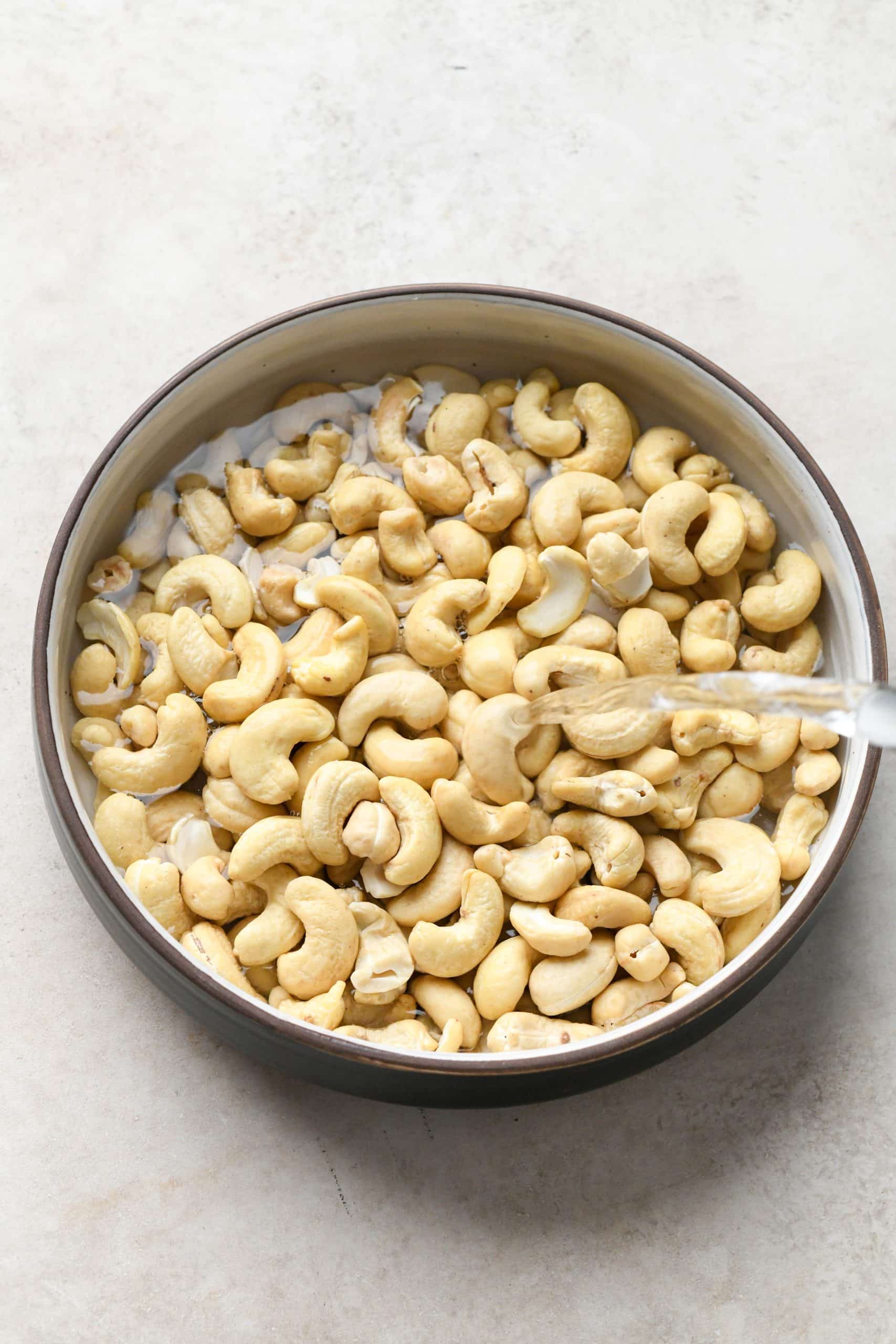 How to make Dairy Free Dill Pickle Dip: Pouring hot water over raw cashews in a shallow bowl.
