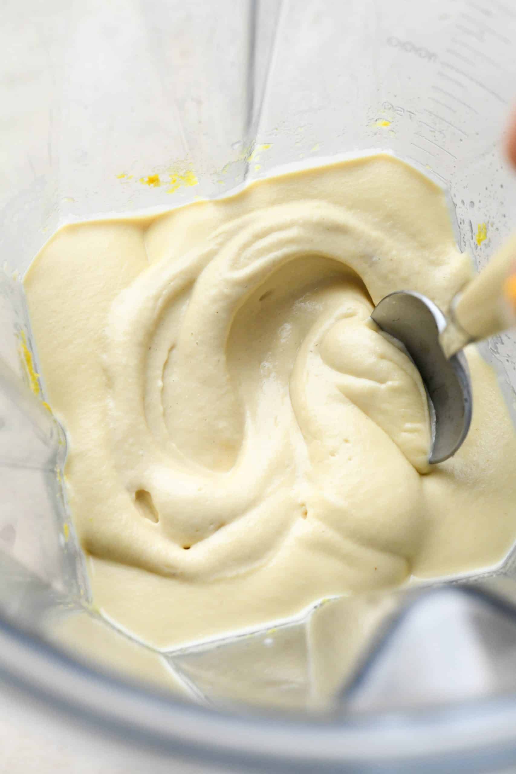 How to make Dairy Free Dill Pickle Dip: Cashew cream blended in blender container with a spoon swirling around the creamy mixture.