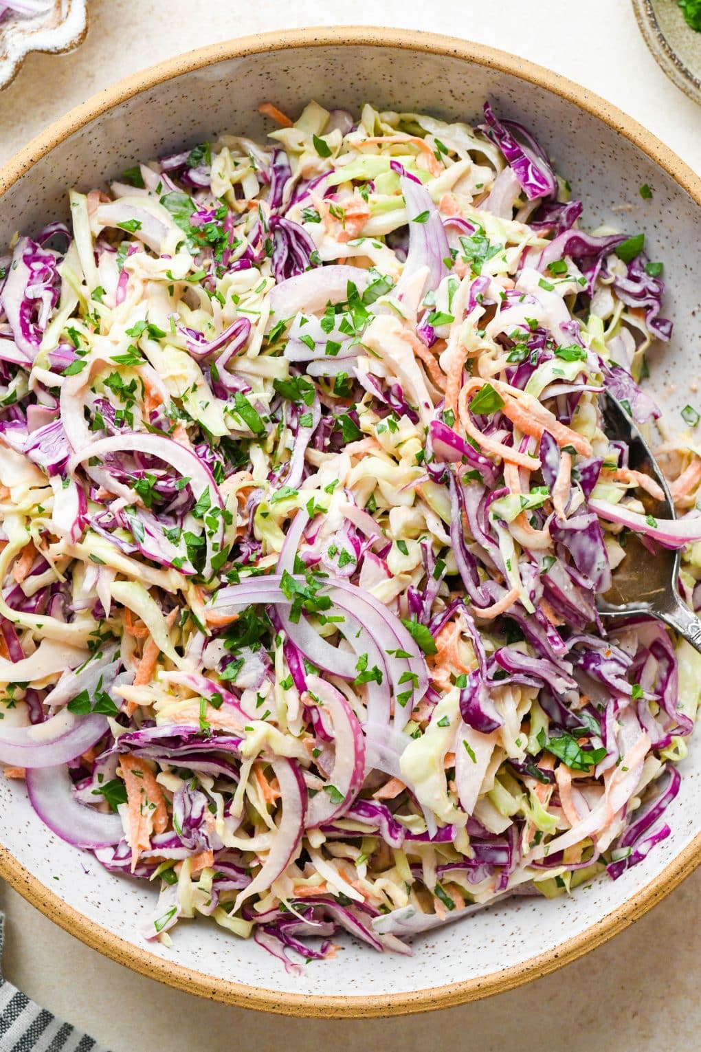 A close up shot of a large serving spoon digging into a bowl of Whole30 coleslaw.