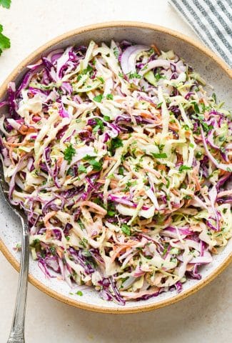 A large white speckled ceramic bowl of creamy Whole30 coleslaw.