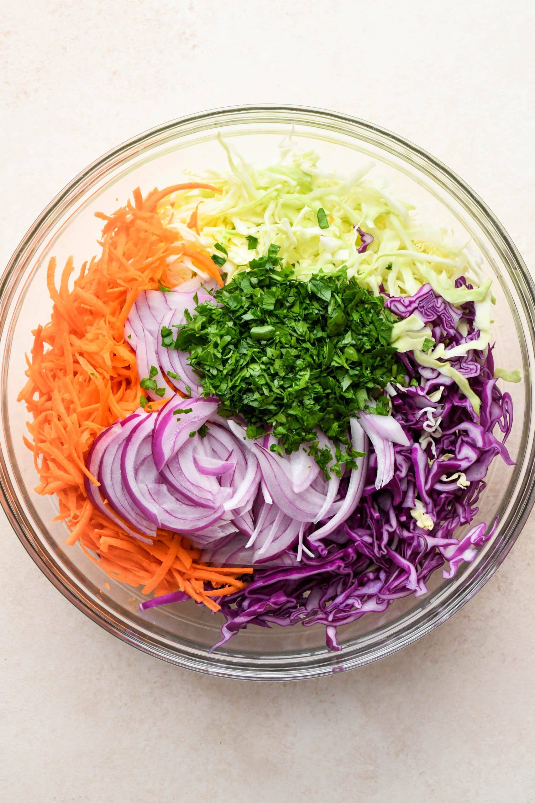 How to make Whole30 coleslaw: Fresh slaw ingredients added to the same glass bowl with the coleslaw dressing.