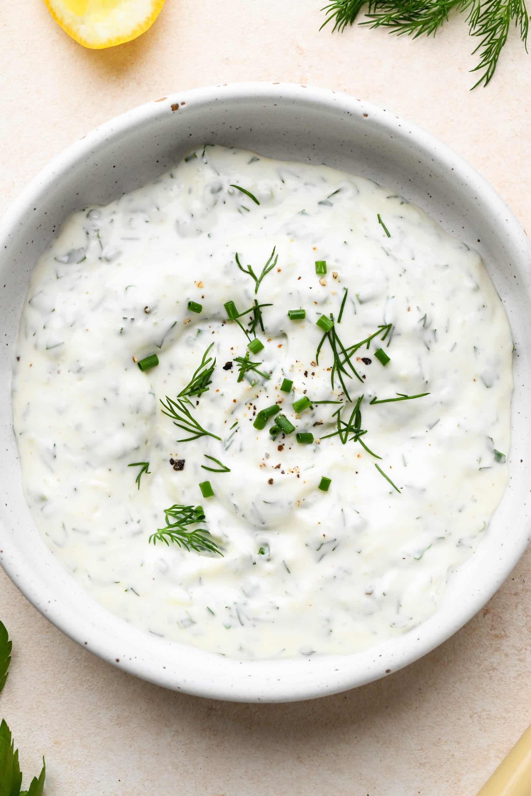 A small shallow ceramic bowl of herb flecked garlic aioli, topped with extra fresh herbs..