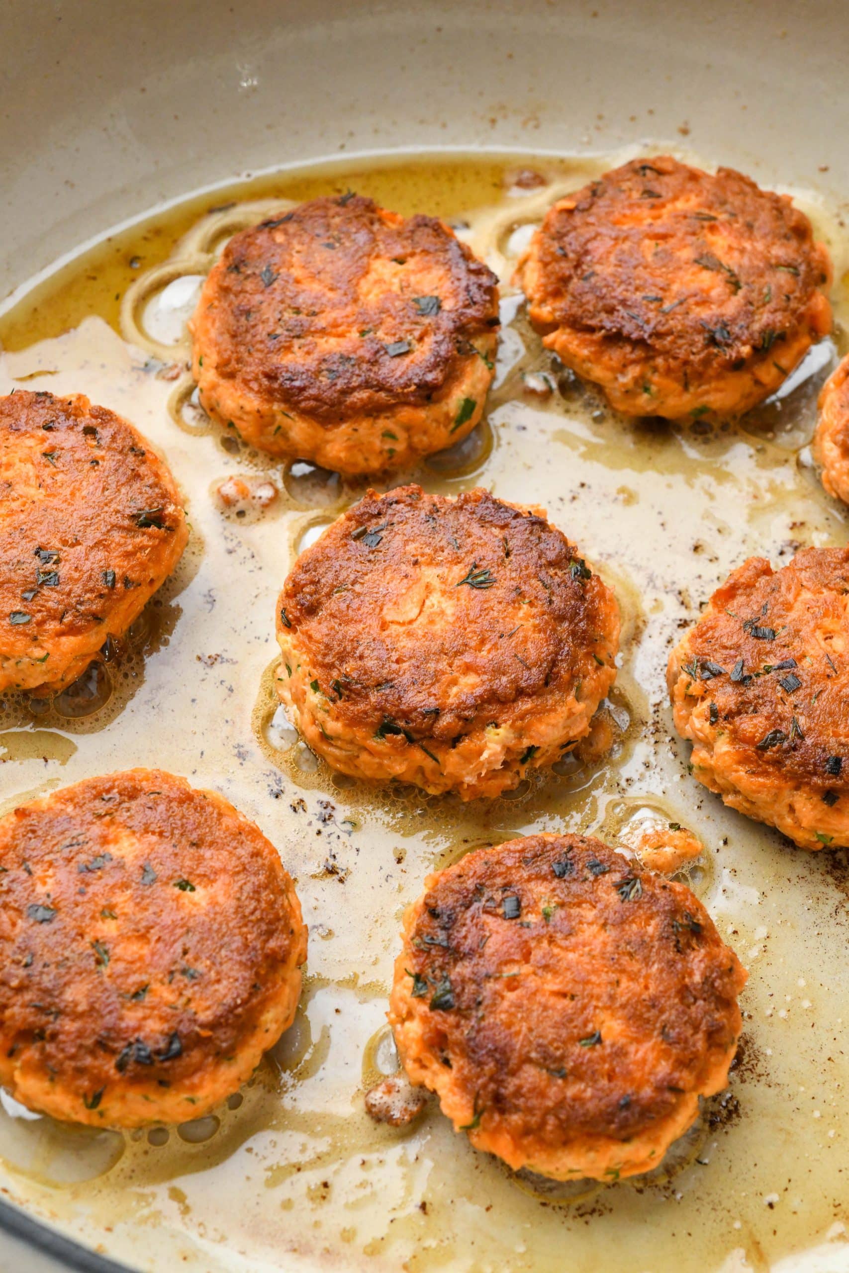 How to make Whole30 Salmon Cakes: Patties cooking in a large white skillet.