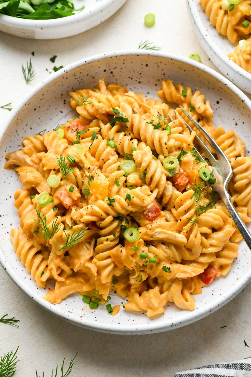 A shallow speckled bowl of creamy dairy free buffalo chicken pasta topped with fresh herbs and a fork angled into the bowl.