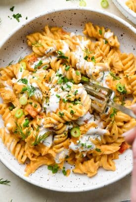 A shallow speckled bowl of creamy dairy free buffalo chicken pasta topped with fresh herbs and dairy free ranch dressing.