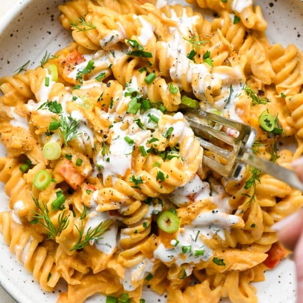 A shallow speckled bowl of creamy dairy free buffalo chicken pasta topped with fresh herbs and dairy free ranch dressing.