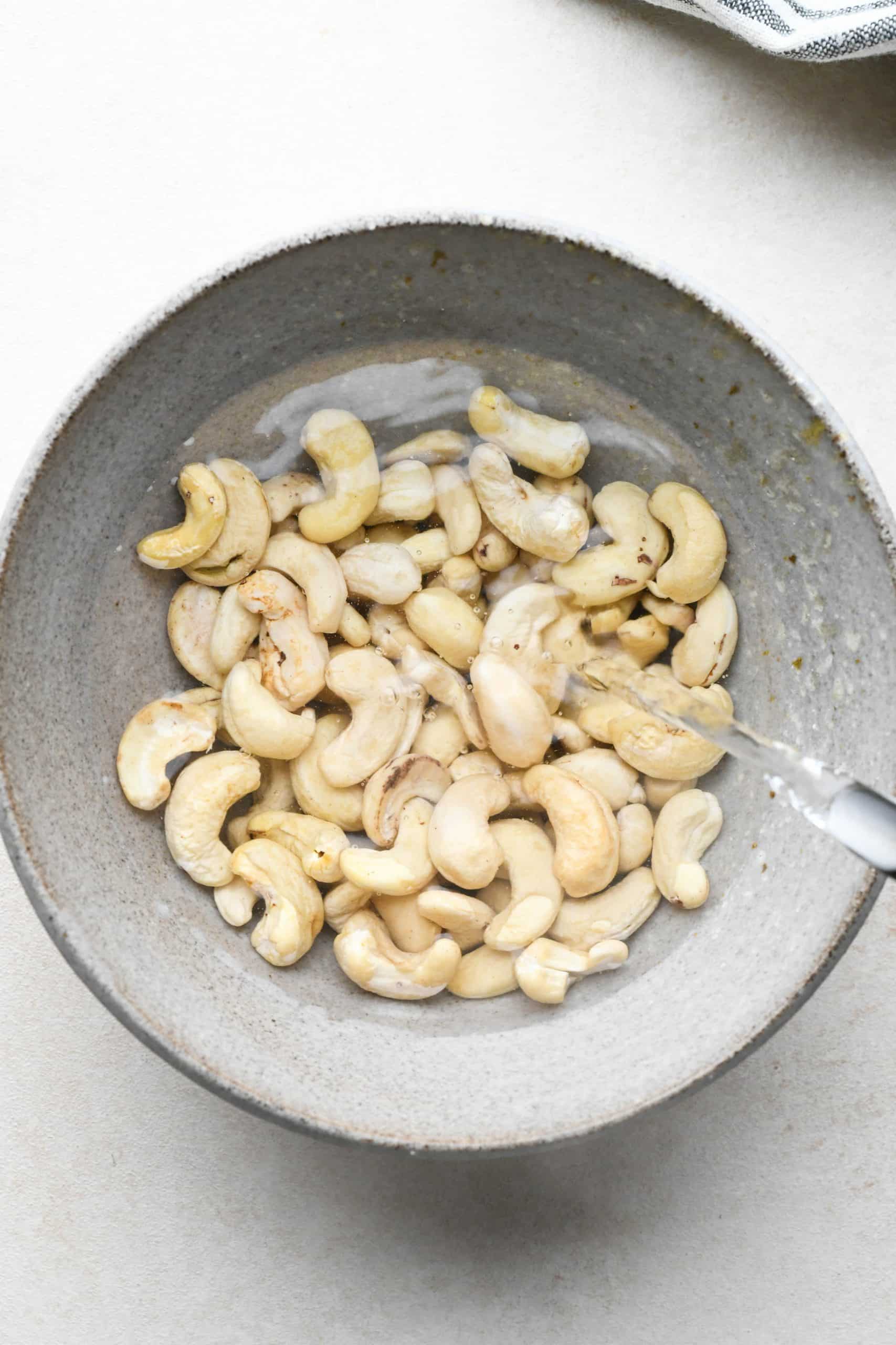 How to make buffalo chicken pasta: Pouring hot water over raw cashews in a small bowl to soak. 