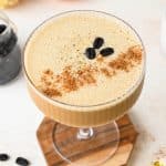 Overhead view of a creamy pumpkin spice espresso martini topped with 3 coffee beans and a dash of pumpkin pie spice, on a creamy background.