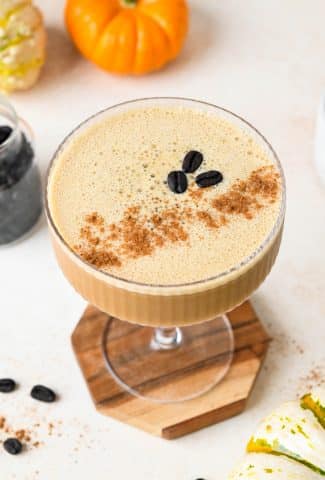 Overhead view of a creamy pumpkin spice espresso martini topped with 3 coffee beans and a dash of pumpkin pie spice, on a creamy background.